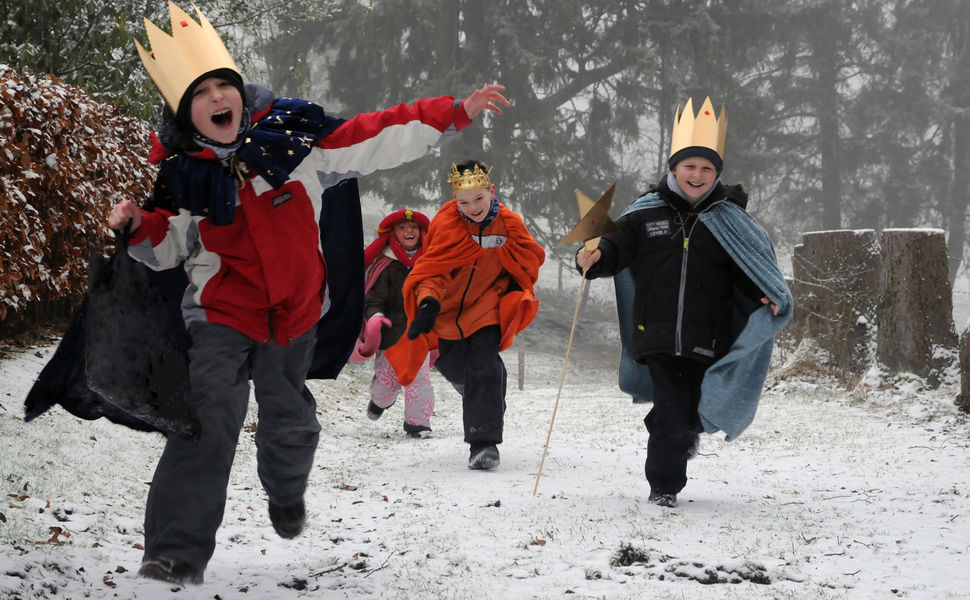 Vier Sternsinger rennen im Schnee auf die Kamera zu.