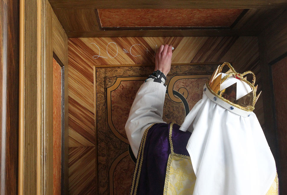 Ein Sternsinger schreibt den Segen 20*C+M ... mit Kreide an eine Holztür an.